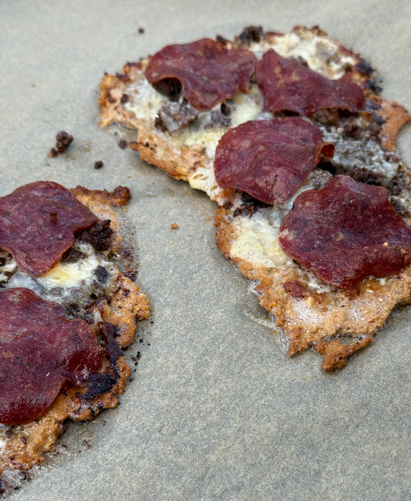 två små pizzor på bakplåtspapper, med gyllenbrun botten, smält ost, köttfärs och skivor av salami ovanpå.